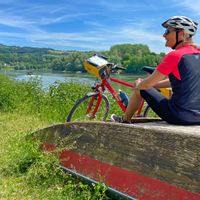 Radlerin bei der Pause sitzend auf einem umgedrehten Boot am Ufer der Donau