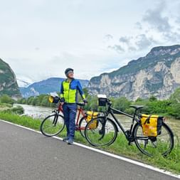 Der Fluss Etsch mit Bergen im Hintergrund und dem Radweg mit Radlern im Vordergrund