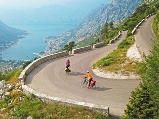 Zwei Radfahrer auf einer Serpentinenstrasse mit Blick auf die von Bergen umgebene Bucht von Kotor