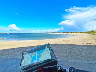 View of the tour map in the bike handlebar bag, sandy beach and sea in the background