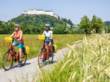 Two cyclists on Hellbrunner Allee in Salzburg, with the fortress in the background