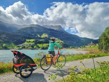 Cycle path at Lake Reschen A cyclist with a child's bike trailer on the shore of Lake Reschen
