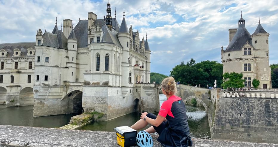 A cyclist sits on a stone wall in front of Chenonceau Castle on the Loire River